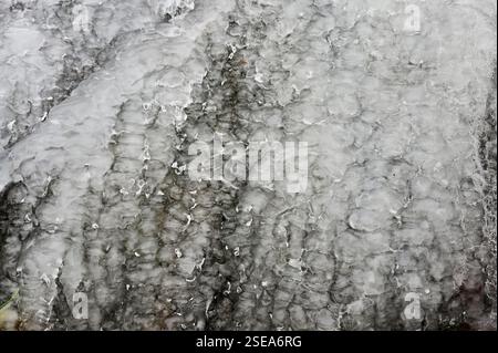 A detailed close-up of an ice-covered surface showcasing intricate patterns and textures formed by frozen water. The ice appears layered, with trapped Stock Photo