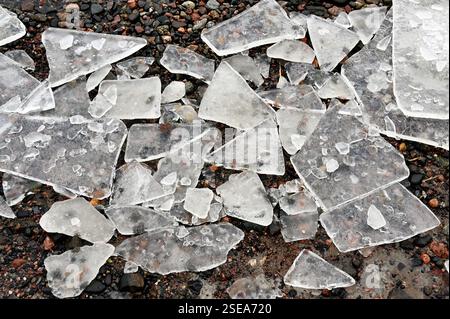 A striking close-up of shattered ice pieces scattered across a rocky surface, highlighting the intricate textures and sharp, jagged edges. The transpa Stock Photo