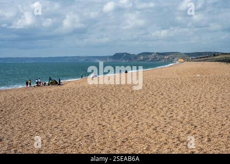 Visitors fish and paddle on Chesil Beach at West Bexington on the shore of Lyme Bay on Dorset's Jurassic Coast. Stock Photo