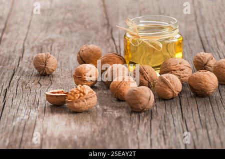 Walnut oil in glass of bottle, whole big peeled walnut kernel with thin shell on wooden background. healthy food for brain. Fresh walnuts background Stock Photo