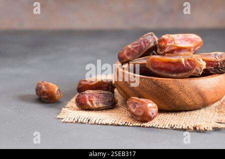 Dates, tasty dry fruit in burlap sack or bowl on wooden rustic background, ramadan kareem food, copy space selective focus (Phoenix dactylifera ) Stock Photo