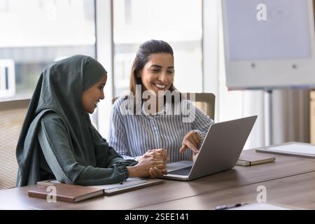 Arabic and Latin businesswomen using laptop in office Stock Photo