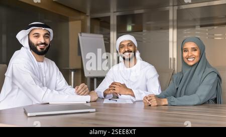 Three professionals sit together at conference table, smiling at camera Stock Photo
