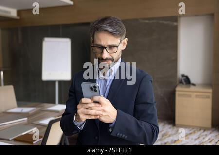 Focused male entrepreneur standing in conference room using his smartphone Stock Photo