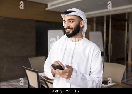 Young successful Arabian businessman dressed in traditional kandura using smartphone Stock Photo