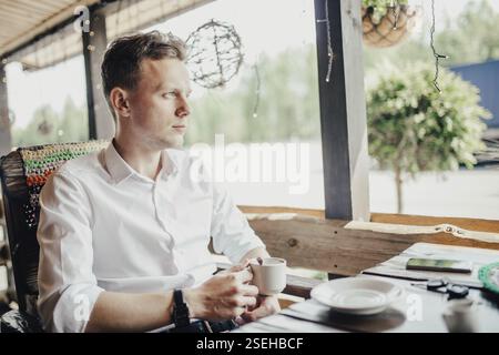 Man sitting on a patio with coffee, surrounded by daytime ambiance Stock Photo