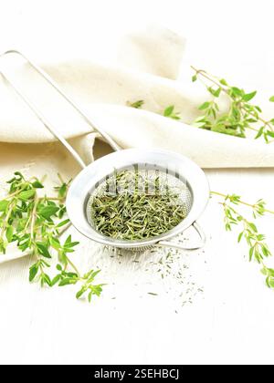 Thyme dry in a metal strainer, fresh greens of grass and linen towel on the background of light wooden boards Stock Photo