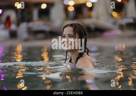 Woman smiling while partially submerged in water with glowing bokeh lights in the background Stock Photo