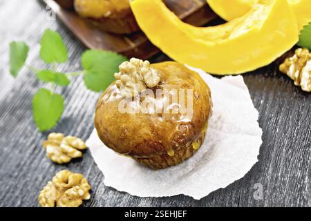 Small pumpkin cupcake with orange glaze and walnut on parchment, mint sprigs on black wooden board background Stock Photo