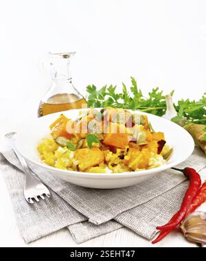 Millet porridge with spicy pumpkin sauce and seeds in a plate on a towel, hot pepper, ginger root, garlic and parsley on white wooden board background Stock Photo