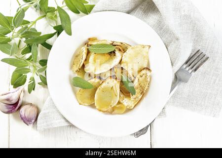 Baked parsnips with spices, garlic and sage in a plate on a napkin on wooden board background from above Stock Photo