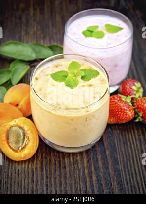 Two glasses of milkshake with apricots, strawberries and mint on the background of a dark wooden board Stock Photo