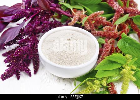 Amaranth flour in a bowl, brown, green and purple flowers and leaves of a plant on the background of light wooden board Stock Photo