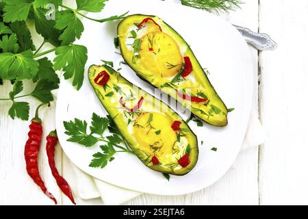 Scrambled eggs with hot peppers in two halves of avocado in a plate, fork, parsley on a wooden background from above Stock Photo