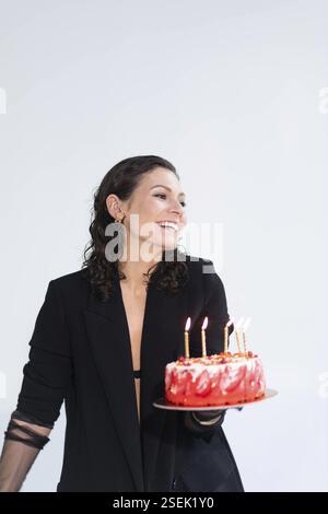 Woman presenting a cake with candles, smiling in celebration Stock Photo