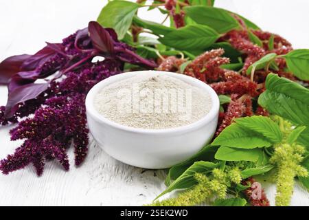 Amaranth flour in a bowl, brown, green and purple flowers and leaves of a plant on wooden board background Stock Photo