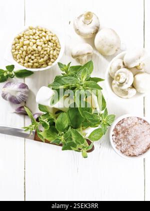 Branches of fresh oregano with green leaves in a mortar, champignons, pink Himalayan salt, pine nuts, garlic and a knife on wooden board background fr Stock Photo