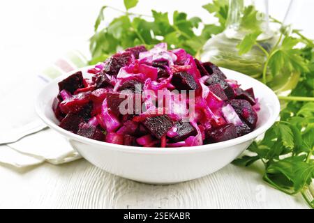 Vinaigrette salad with pickled or sauerkraut, potatoes, beetroot and onion, seasoned with vegetable oil in a bowl, towel, parsley on a wooden board ba Stock Photo