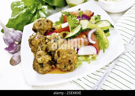 Minced meatballs with spinach, oatmeal and green onions in tomato sauce, vegetable salad in a plate, towel on white wooden board background Stock Photo