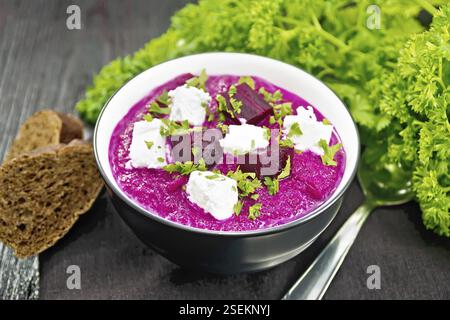 Soup puree of beetroot, potato and cream with salted cream cheese in a bowl on towel, bread and parsley on wooden board background Stock Photo