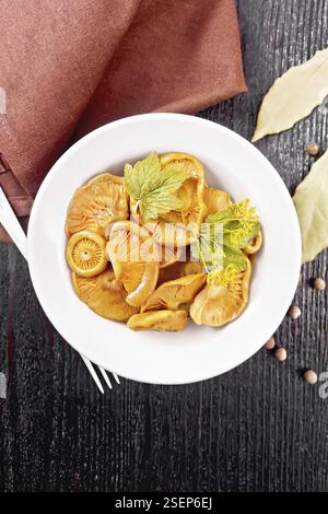 Salted mushrooms saffron with sour cream, currant leaf and sprig of dill in plate, fork, napkin, bay leaf and pepper on wooden board background from a Stock Photo