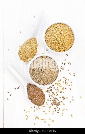 Flaxseed flour in a bowl, white and brown linen seeds in two spoons and on table on wooden board background from above Stock Photo