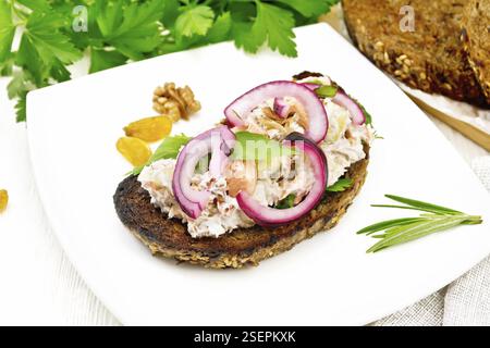 Salad of salmon, petiole celery, raisins, walnuts, red onions and cottage cheese on toasted bread with green lettuce on a plate on a white wooden boar Stock Photo