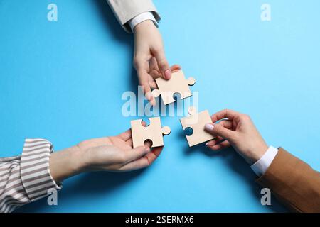 Business strategy and teamwork concept. Partners with different puzzle pieces on light blue background, top view Stock Photo