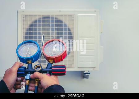 Air repair mechanic using measuring equipment for filling industrial factory air conditioners and checking maintenance outdoor air compressor unit. Stock Photo