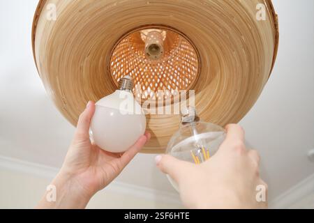 Female hands change an incandescent lamp for an energy-saving lamp in a large wooden chandelier Stock Photo