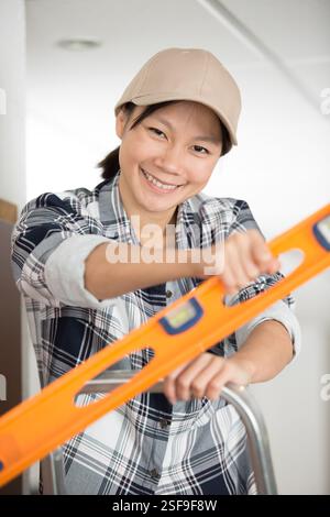 female builder on stepladder holding a spirit level Stock Photo