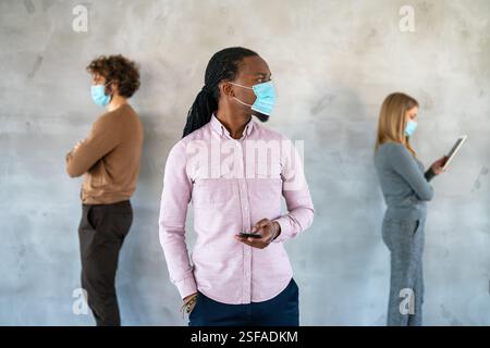 People in business style and medical masks standing with gadgets and keeping social distance. Stock Photo