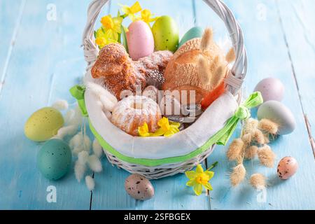 Stylish Easter basket with flowers, painted eggs and bread. Easter food for blessing in church. Stock Photo