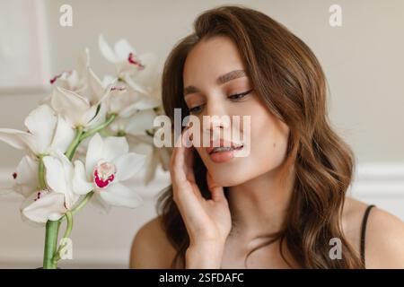 Close-up portrait of a beautiful young woman sitting in a living room next to white boat orchids Stock Photo