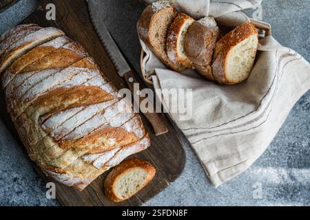 Close-up of Freshly sliced  sourdough bread in a bread basket next to a sliced loaf of brad on a chopping board Stock Photo