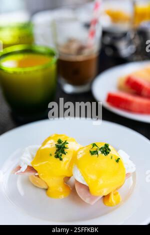 Close-up of two eggs Benedict on a white plate, topped with rich yellow hollandaise sauce and garnished with parsley, served at a breakfast table Stock Photo