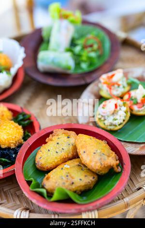 An assortment of traditional Vietnamese snacks including fried banana fritters, spring rolls, and shrimp-topped rice cakes, all served on colorful pla Stock Photo