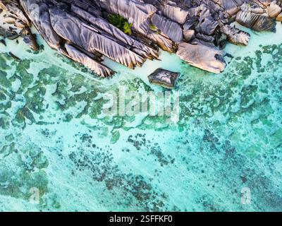 An aerial view of Anse Source d'Argent's granite rock formations and shallow, turquoise waters with visible reef patterns on La Digue, Seychelles Stock Photo
