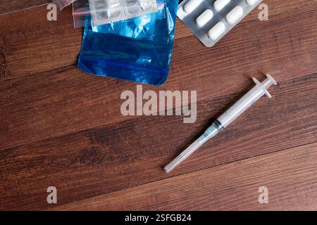 A syringe and various medication packages on a wooden surface, depicting themes of healthcare, medication, and drug use. Stock Photo