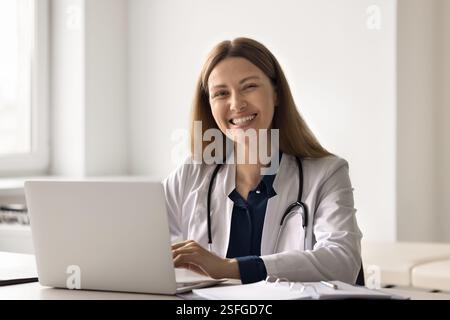 Young doctor sitting at desk by notebook looking at camera Stock Photo