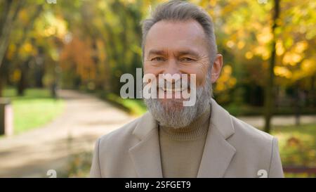 Portrait senior Caucasian male intelligent 60s old man happy retired bearded grandpa in city park satisfied joyful middle age gentleman looking at Stock Photo
