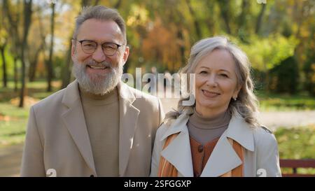 Happy family portrait in autumn park city outdoors retired Caucasian couple mature husband wife man woman elegant spouses looking to camera smiling Stock Photo
