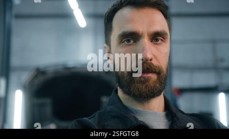 Serious adult bearded man Caucasian guy confident male industrial worker in uniform technician engineer repairman automobile mechanic looking at Stock Photo