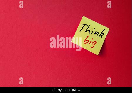 Think big symbol. Orange steaky note with words Think big. Beautiful red background. Business and Think big concept. Copy space. Stock Photo