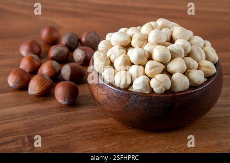Hazelnut kernels in a wooden bowl with a group of shelled hazelnuts on the table Stock Photo