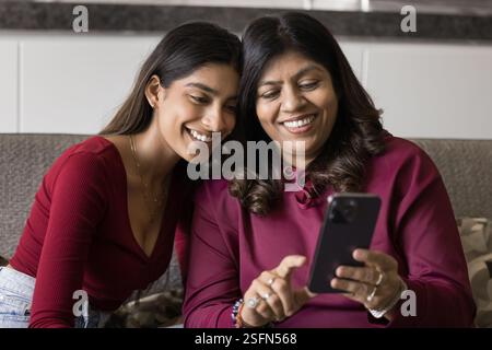 Smiling Indian woman and daughter using smartphone Stock Photo