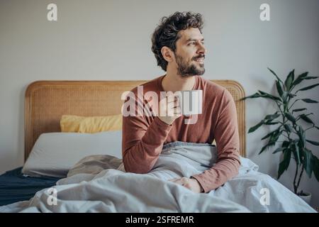 Relaxed Young handsome middle eastern man Enjoying Morning Coffee in Bed. Stock Photo
