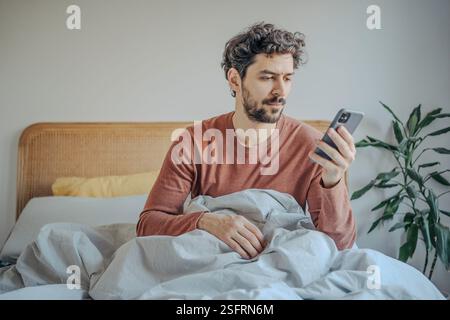 Relaxed Morning Routine – Young handsome middle eastern bearded Man in Bed Checking Phone . Stock Photo