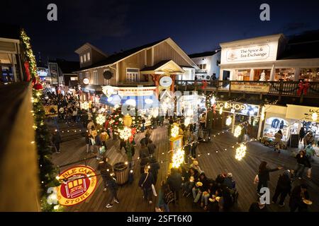 Pier 39 in San Francisco, CA, at night.  Holiday shoppers enjoy festive treats and shops.  Christmas decorations and lights are prominent. Stock Photo