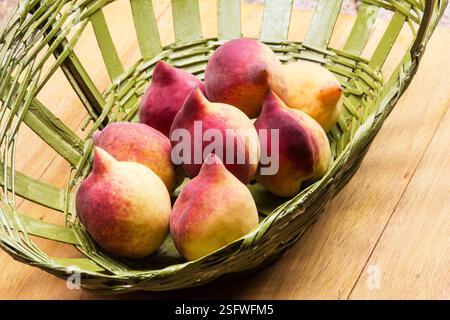 Fresh beautiful peaches (Prunus persica) in a basket on a wooden background Stock Photo